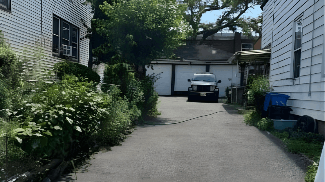 Driveway and rear view of the multi family property at 72-74 Maple St in Paterson NJ showing the private parking area, greenery, and 3 car garage.