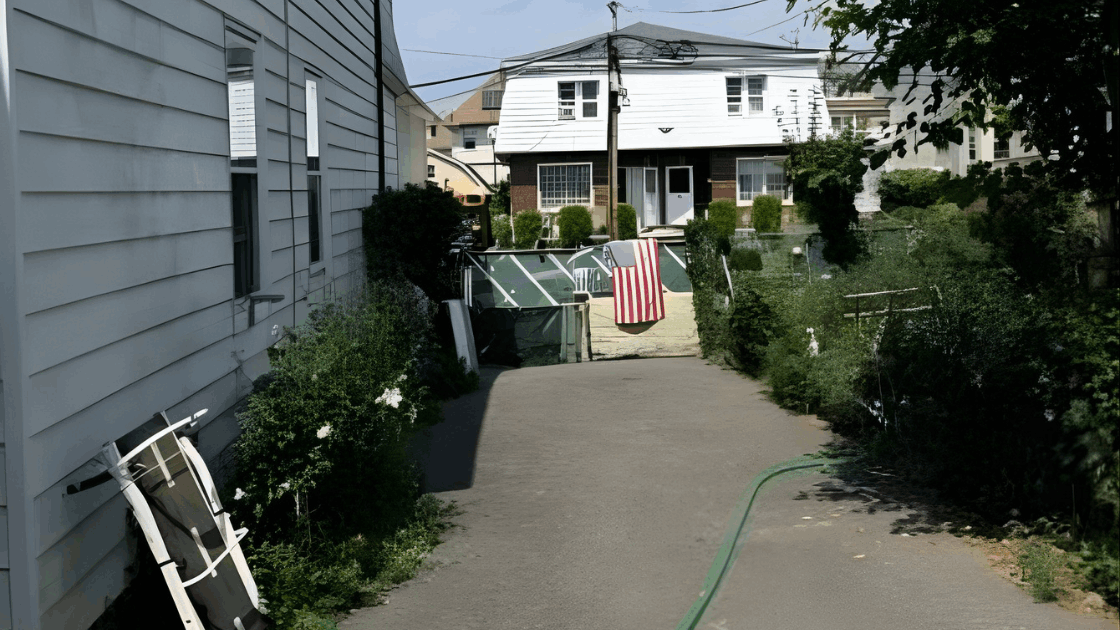 Driveway and rear view of the multi family property at 72-74 Maple St in Paterson NJ showing the private parking area, greenery, and 3 car garage.