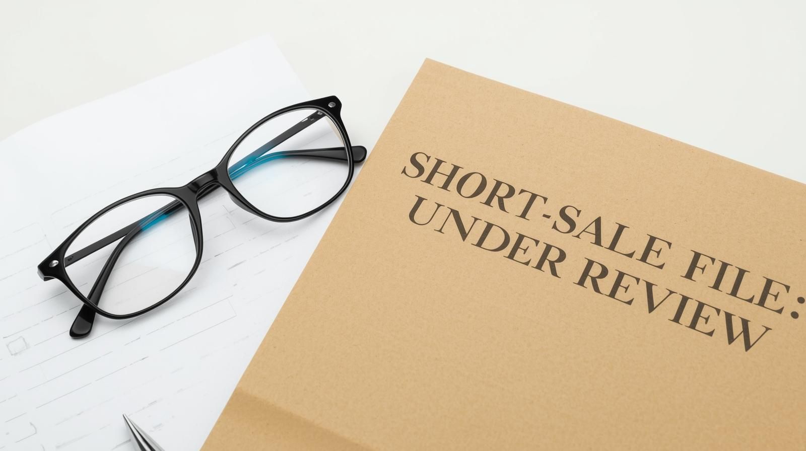 Folder labeled &ldquo;Short-Sale File: Under Review&rdquo; with glasses resting on financial documents, representing the lender review process during a short sale.