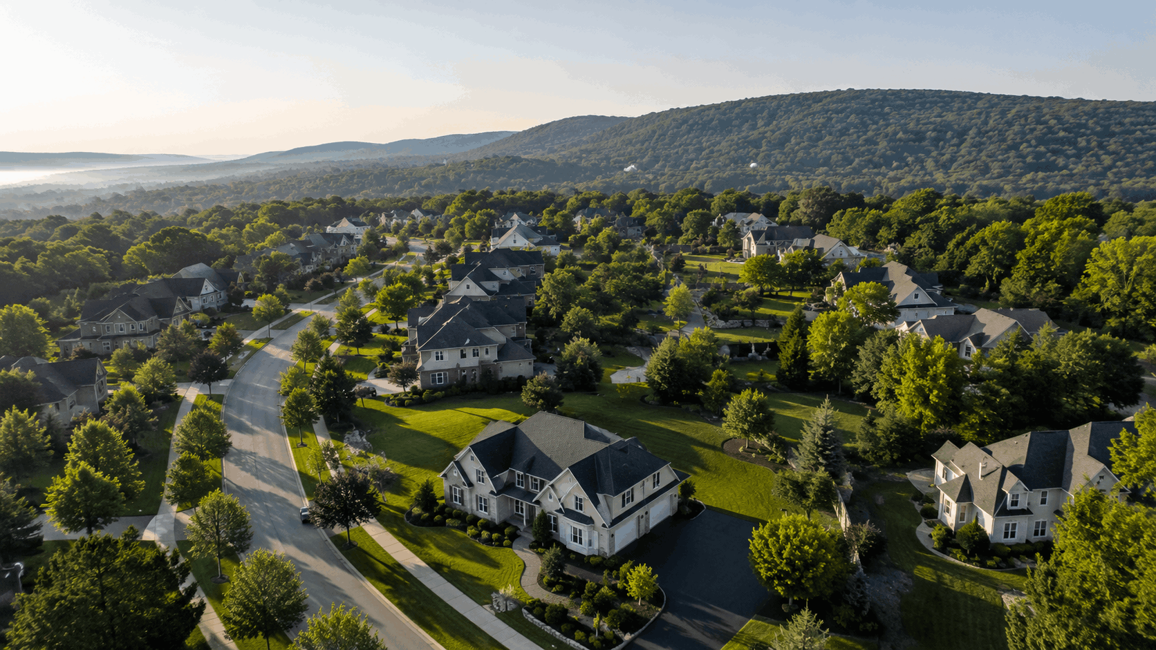Aerial view of a peaceful North Haledon, NJ neighborhood with spacious homes, green lawns, tree-lined streets, and wooded hills.