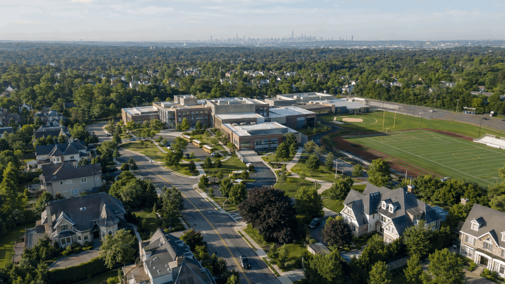 Aerial view of a North Jersey school district with suburban homes, athletic fields, school buses, and the Manhattan skyline.