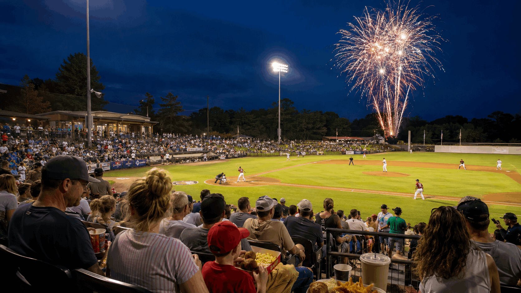 Families watch a summer baseball game in Augusta, New Jersey, with stadium lights, refreshments, and postgame fireworks.