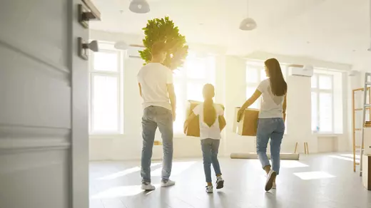 Family moving into a bright, modern home carrying boxes and a houseplant—sunlight streaming through large windows, symbolizing a fresh start with Homes With Monika, Arizona real estate expert.
