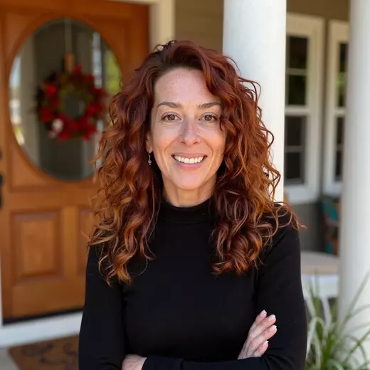 Monika La Vigna, Arizona REALTOR® with long curly red hair, smiling confidently in front of a welcoming entryway with a holiday wreath—trusted local expert at Homes With Monika.