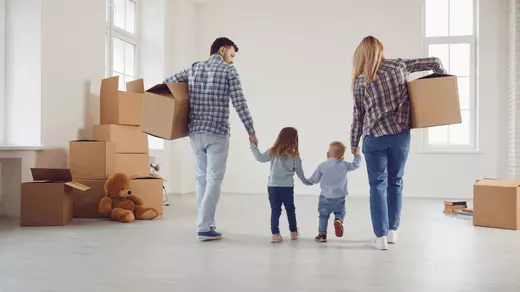 oung family with two children moving into a new home, carrying boxes into a bright, empty living room—creating new beginnings with Homes With Monika, Arizona real estate expert.