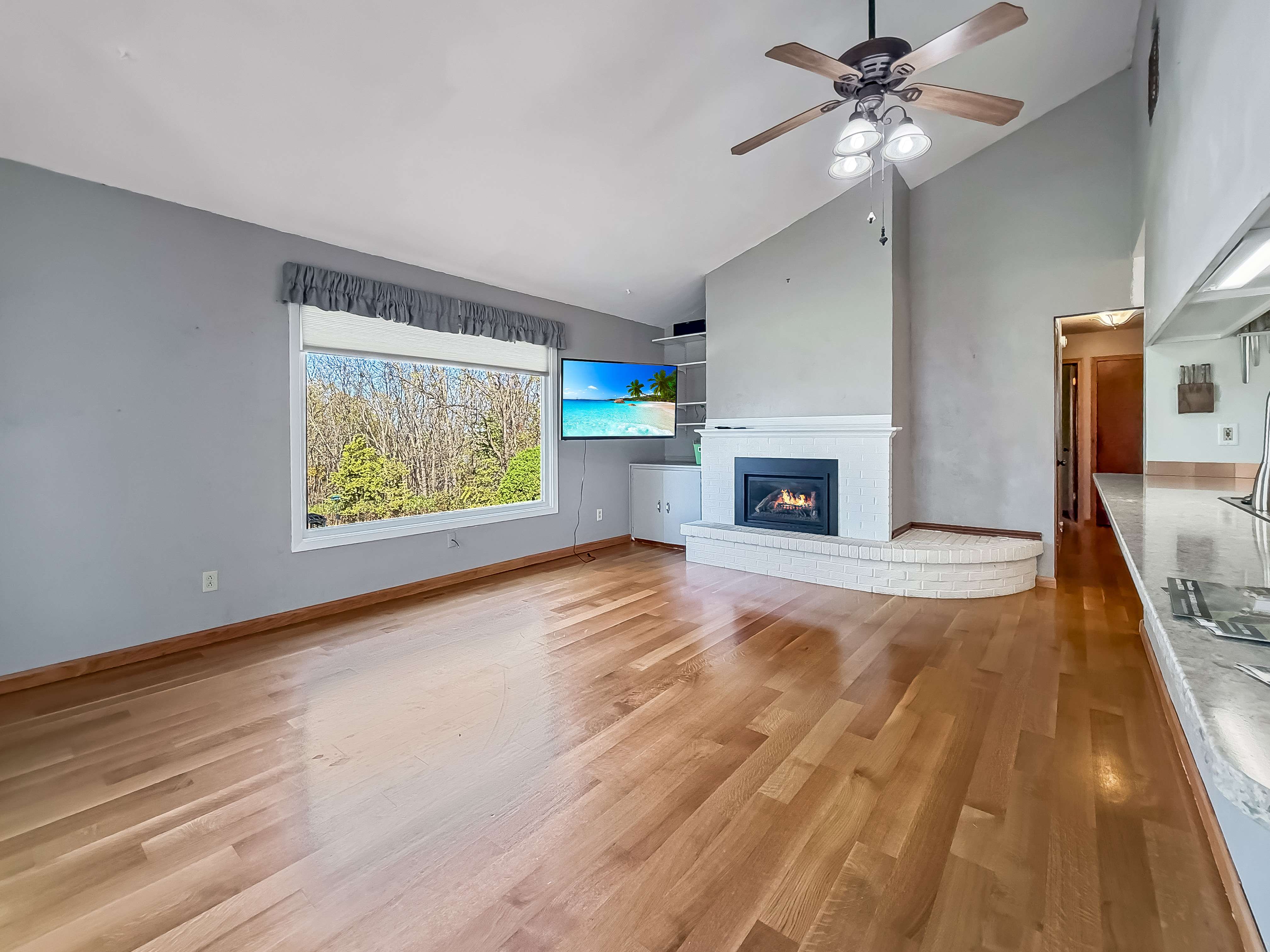 Vaulted living room with hardwood floors and a white brick wood-burning fireplace