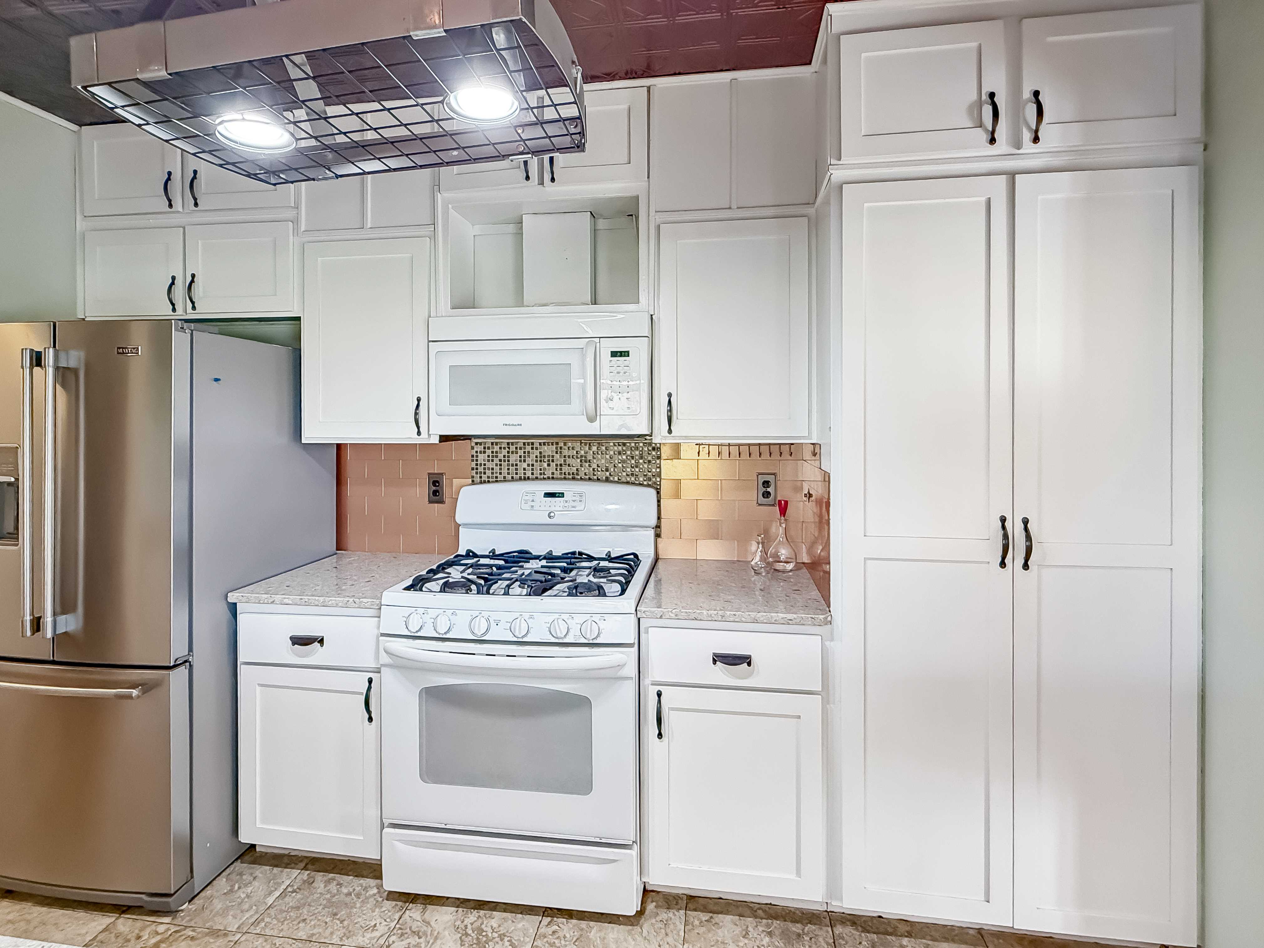 Kitchen with white shaker cabinets, stainless refrigerator and range