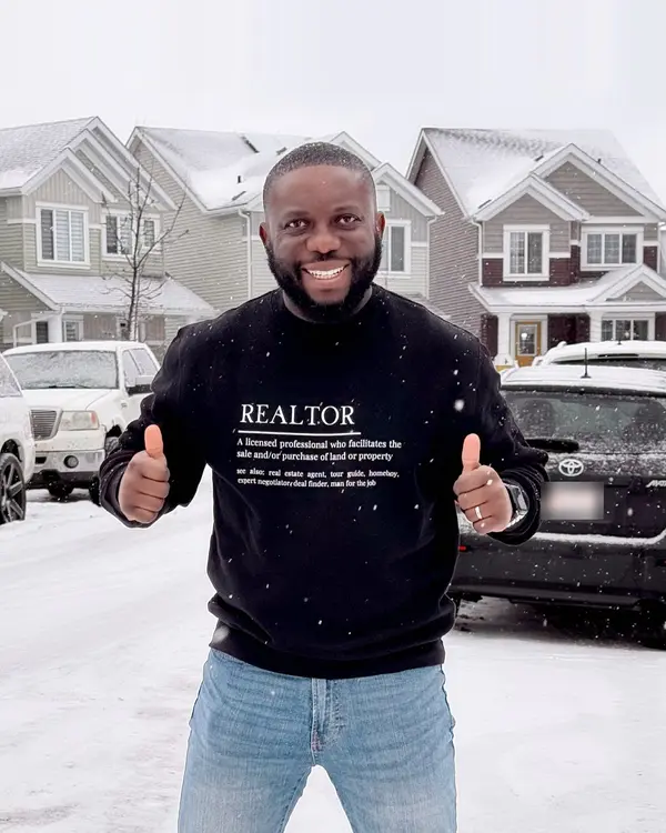 DK Shittu, Edmonton REALTOR® with LPT Realty, giving a thumbs-up on a snowy residential street in a black REALTOR sweater