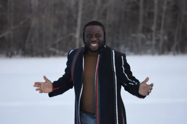 DK Shittu, Edmonton REALTOR® with LPT Realty, smiling with arms open in a winter coat in a snowy field