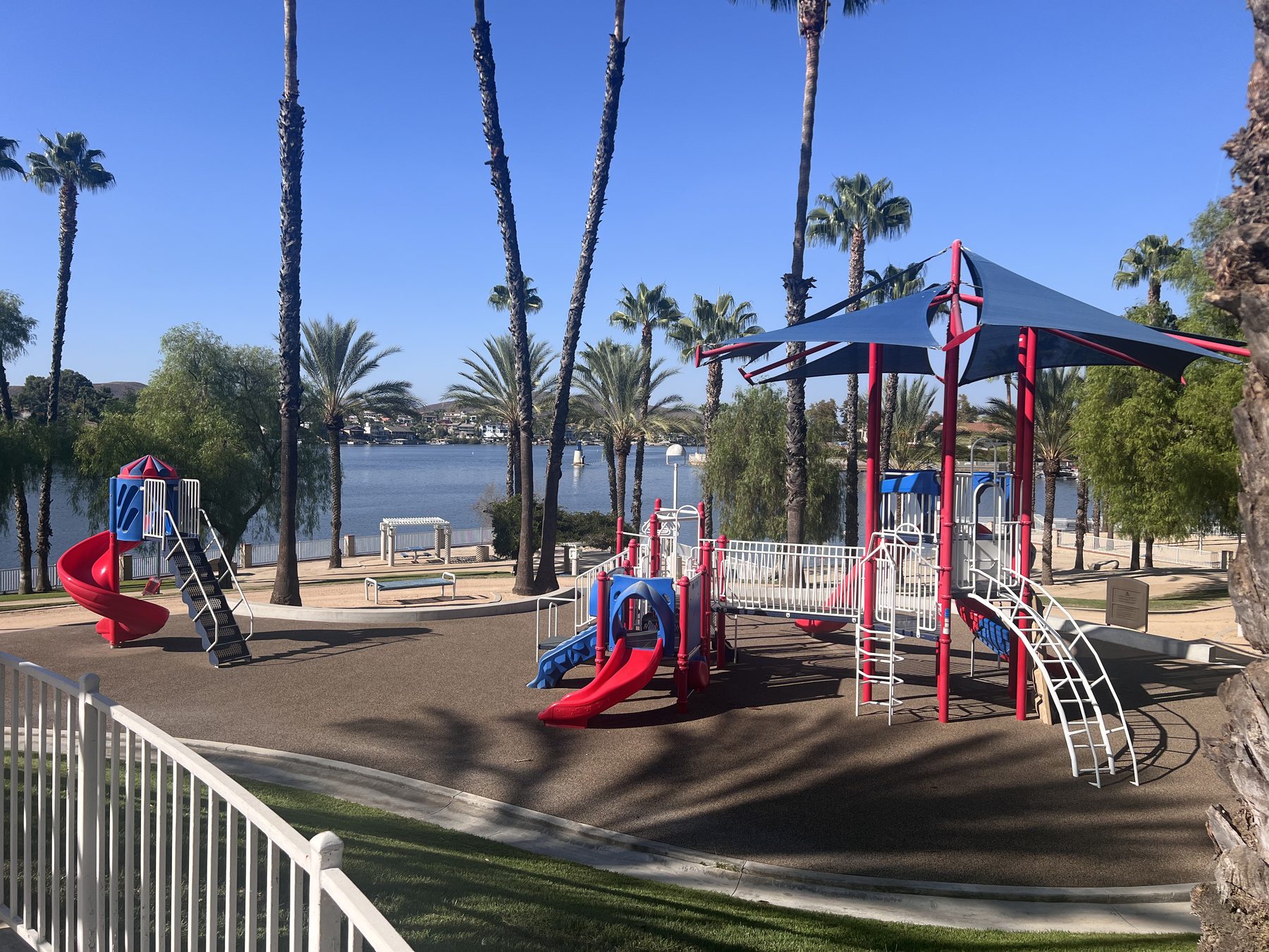 A lakeside playground at Canyon Lake, shaded by palms with the main lake directly behind it.