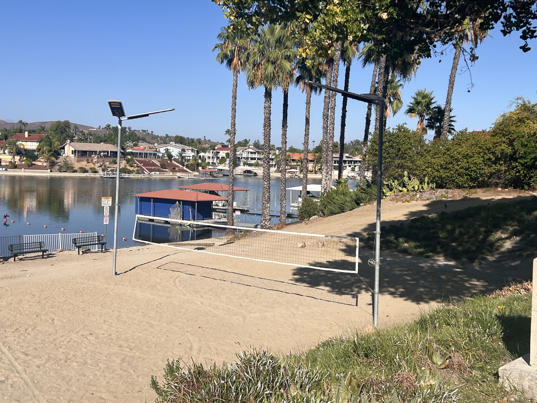 A beach volleyball court on the sand at Canyon Lake, with the lake and waterfront homes beyond.