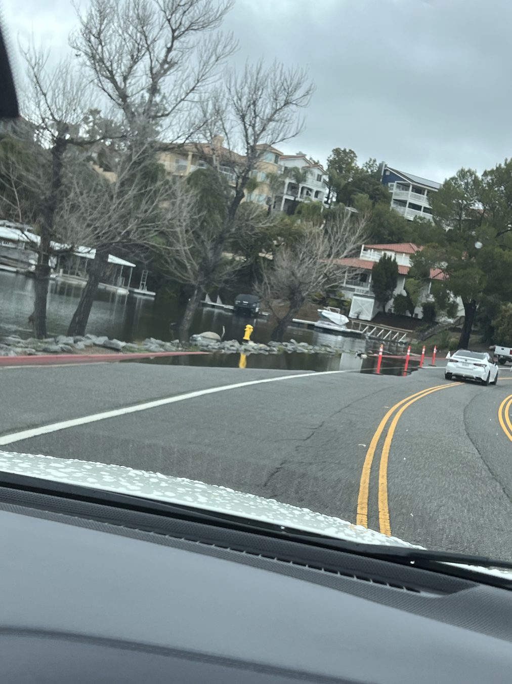 The causeway at Canyon Lake in February 2024, with floodwater up to the edge of the roadway and traffic cones in place.