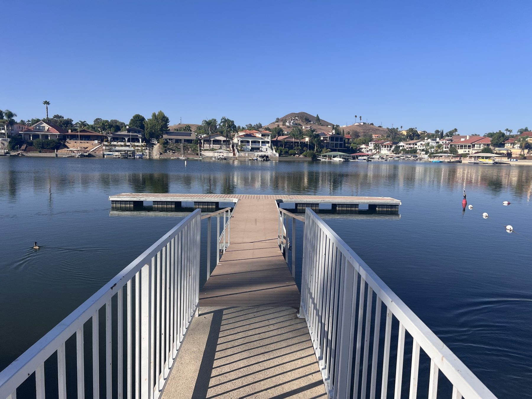 A gangway leading out to a private floating dock on Canyon Lake, with waterfront homes and hills across the water.