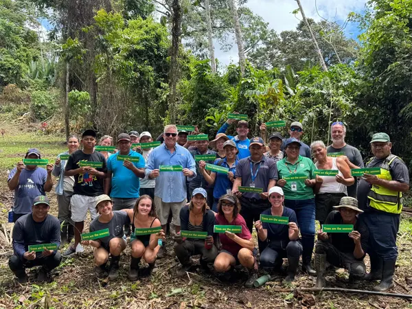 Rotary volunteers and local community members in Panama holding "Trees are the answer" stickers at a reforestation site