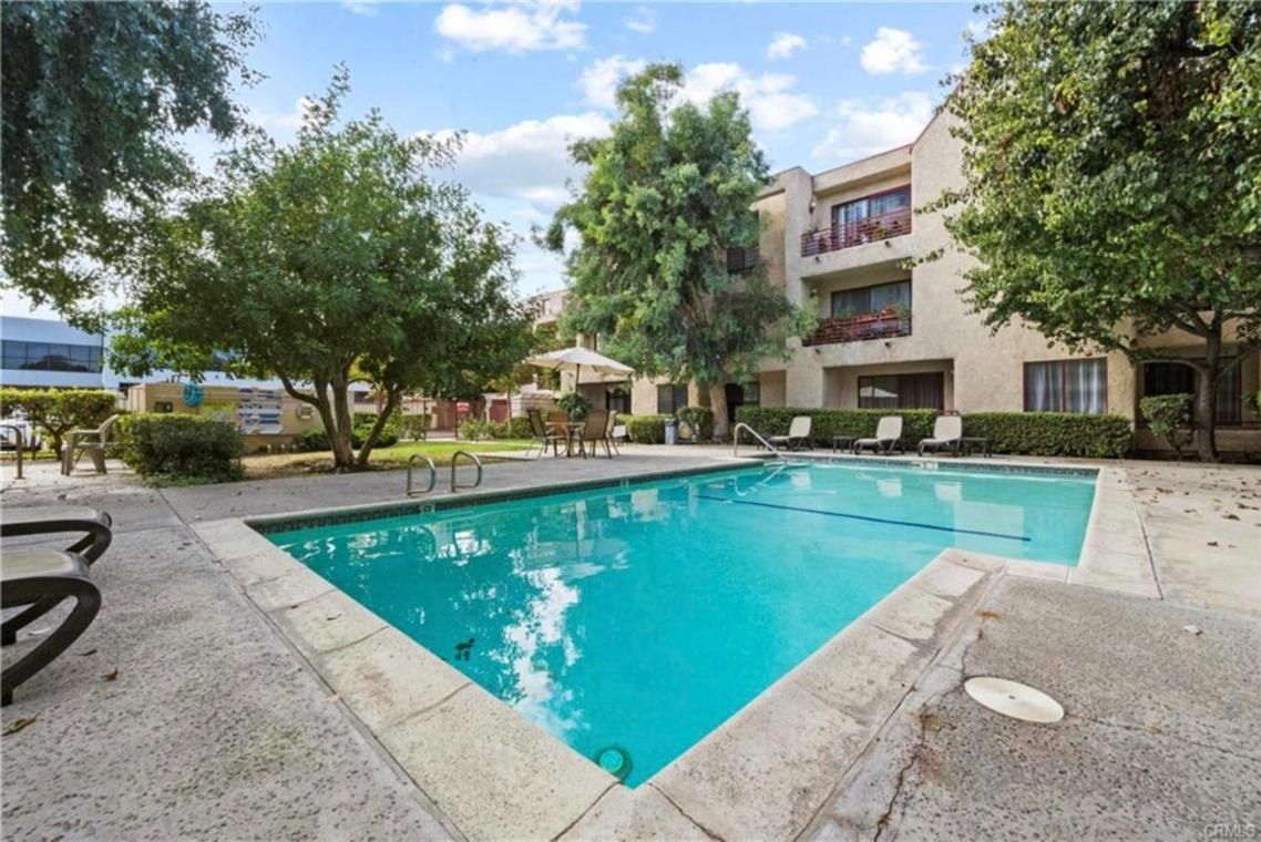 Pool at Warner Gardens condos with lounge chairs and the three-story building behind