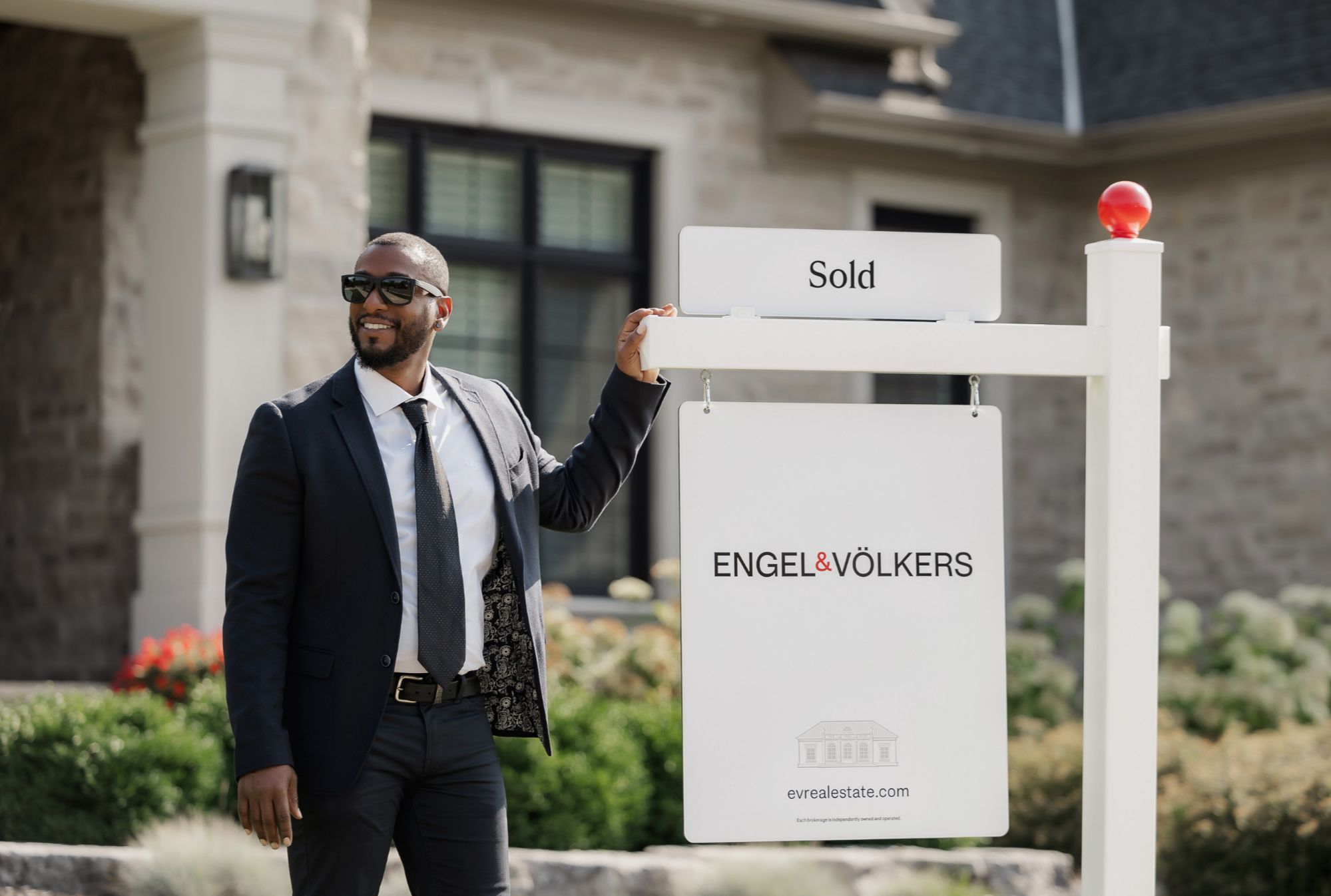 Engel & Völkers real estate advisor confidently standing by a sold sign in front of a Kaneohe home.