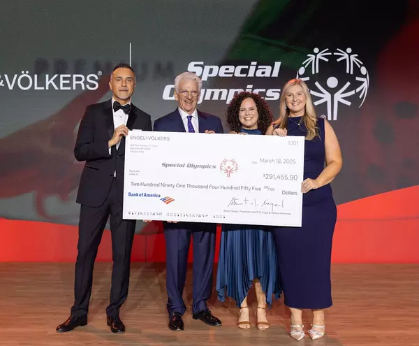 Engel & Völkers executives present a $291,455.90 donation check to Special Olympics on March 18, 2025, during a formal event, standing on stage in front of a branded backdrop.