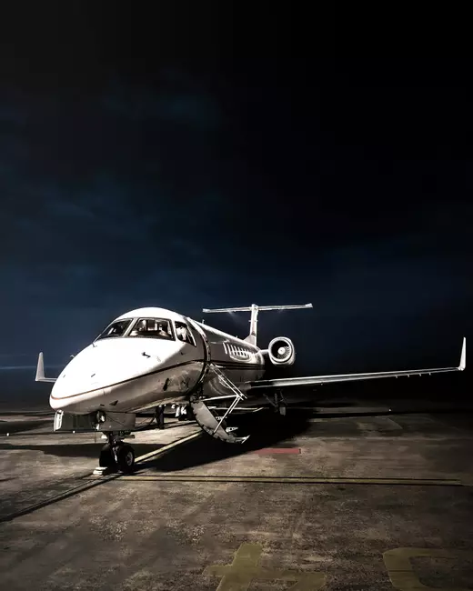 Luxury private jet on runway under dramatic night sky, representing Engel & Völkers Aviation charter and aircraft sales services.