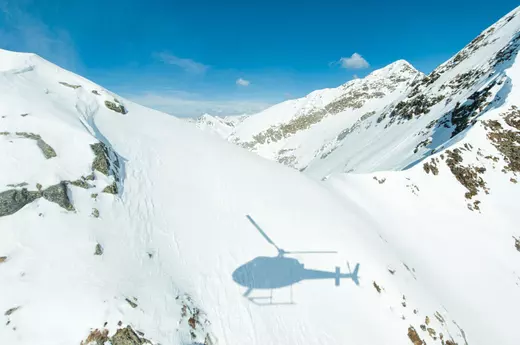 Helicopter flying above snow-covered alpine mountains, showcasing Engel & Völkers Aviation lifestyle and exclusive flight experiences.