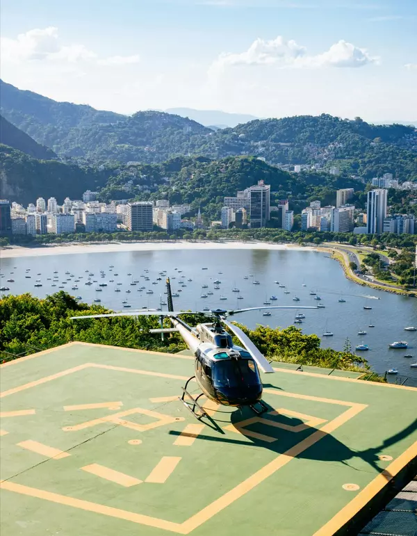 Luxury helicopter on a rooftop helipad overlooking Rio de Janeiro’s coastline and marina, representing Engel & Völkers Aviation lifestyle