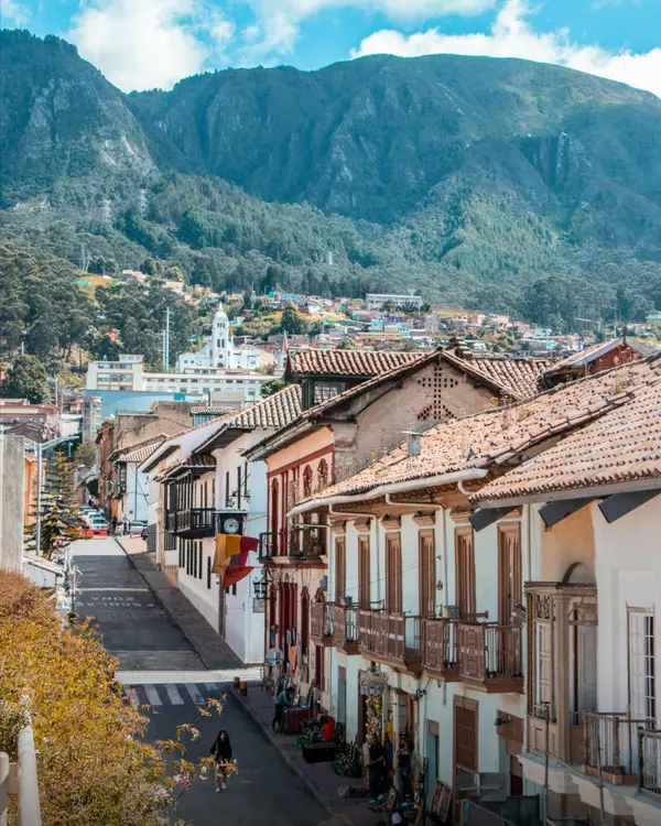Colorful colonial street in Bogotá, Colombia with historic balconies and mountain views in the background, showcasing the charm of Andean architecture and urban lifestyle.