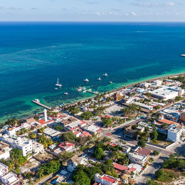 Aerial view of Puerto Morelos coastline with turquoise Caribbean waters, boats anchored near the pier, and colorful beachfront homes along Mexico’s Riviera Maya.