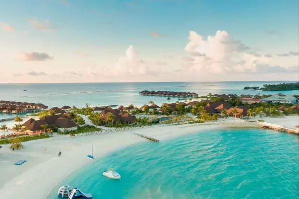 Aerial view of luxury beachfront villas along turquoise Caribbean waters with white-sand beaches and tropical palm trees at sunset.