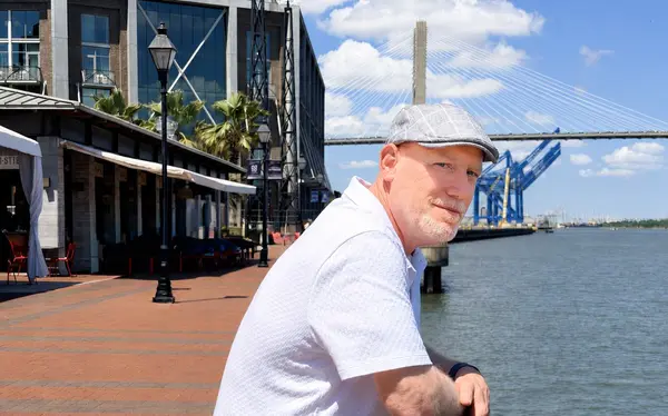 Man Standing Next to River with Port in the Background