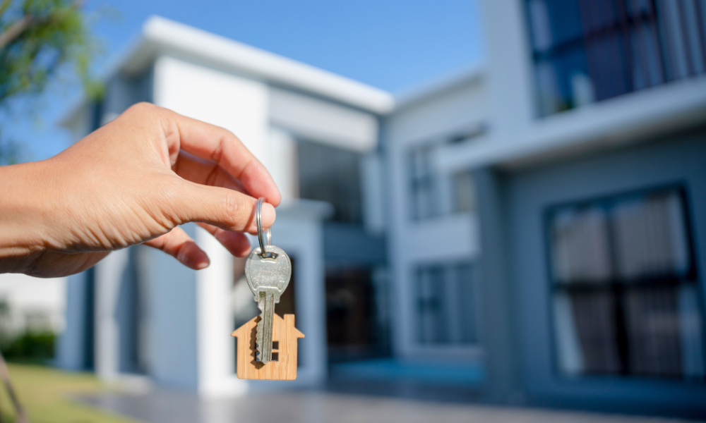 Hand holding keys in front of new home 