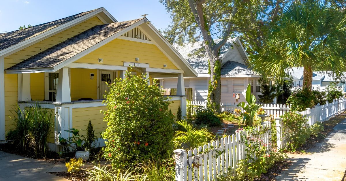 Yellow craftsman bungalow with a wraparound porch and white picket fence on a tree-lined street in Harbordale, St. Petersburg, FL