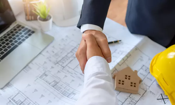 Two men shaking hands over construction blueprint