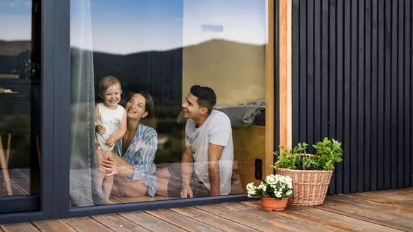 Smiling family with young child looking outside through large glass door of their modern home