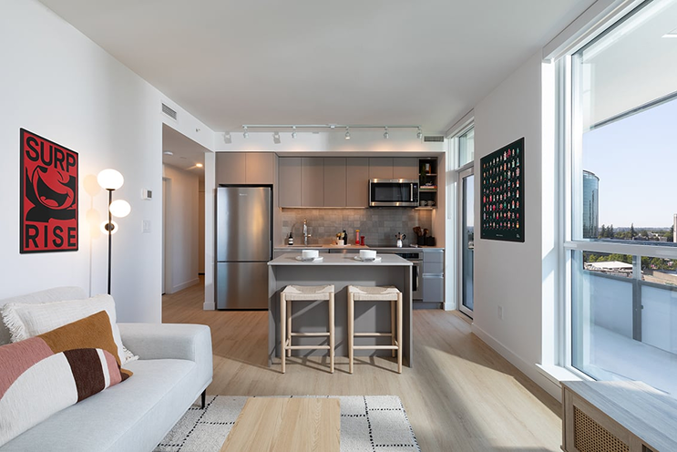 Parkway condo interior render by Bosa Properties showing kitchen with grey cabinetry, stainless steel appliances, waterfall quartz island, and floor-to-ceiling windows