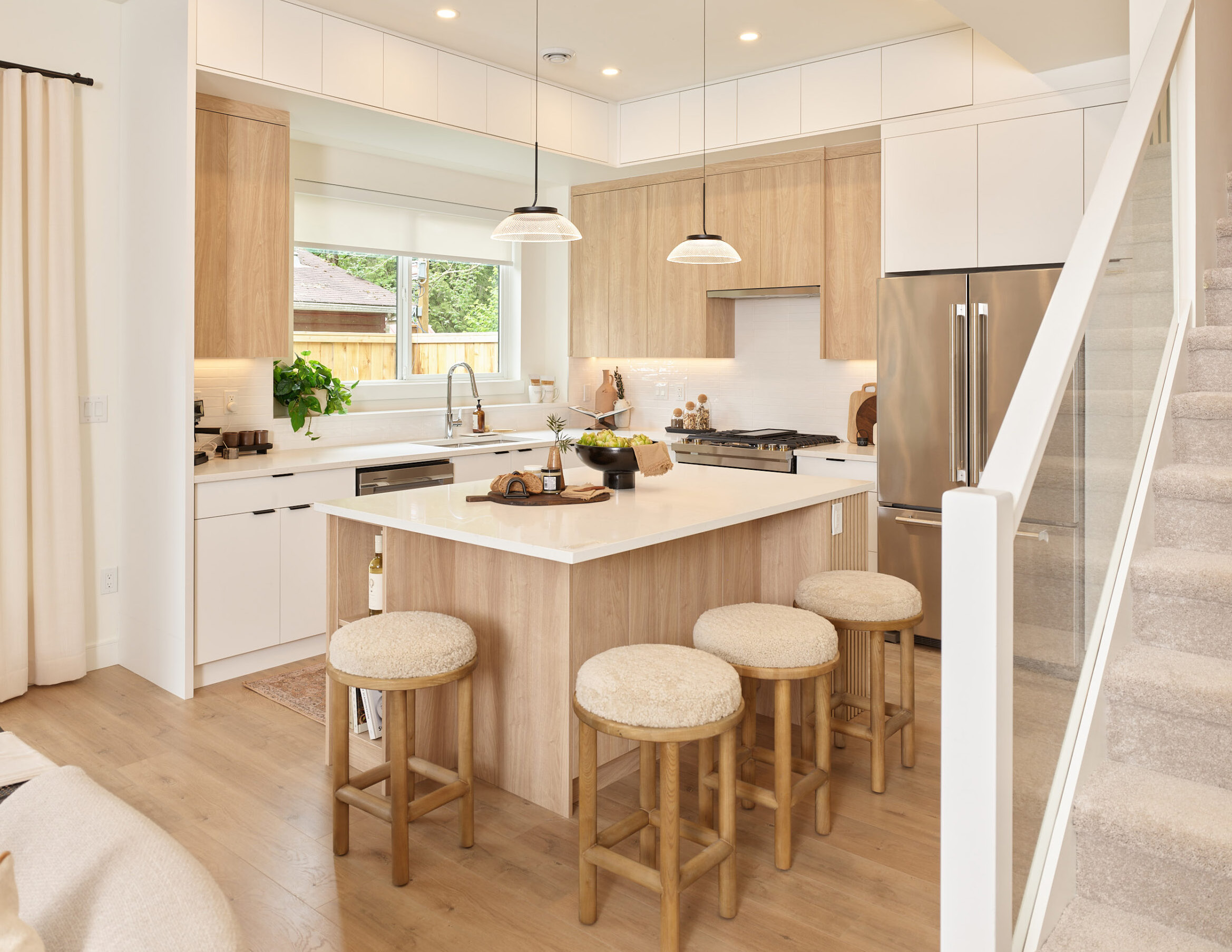 Everwood townhome kitchen with oversized island, light wood cabinetry, quartz waterfall counters, stainless appliances, and pendant lighting