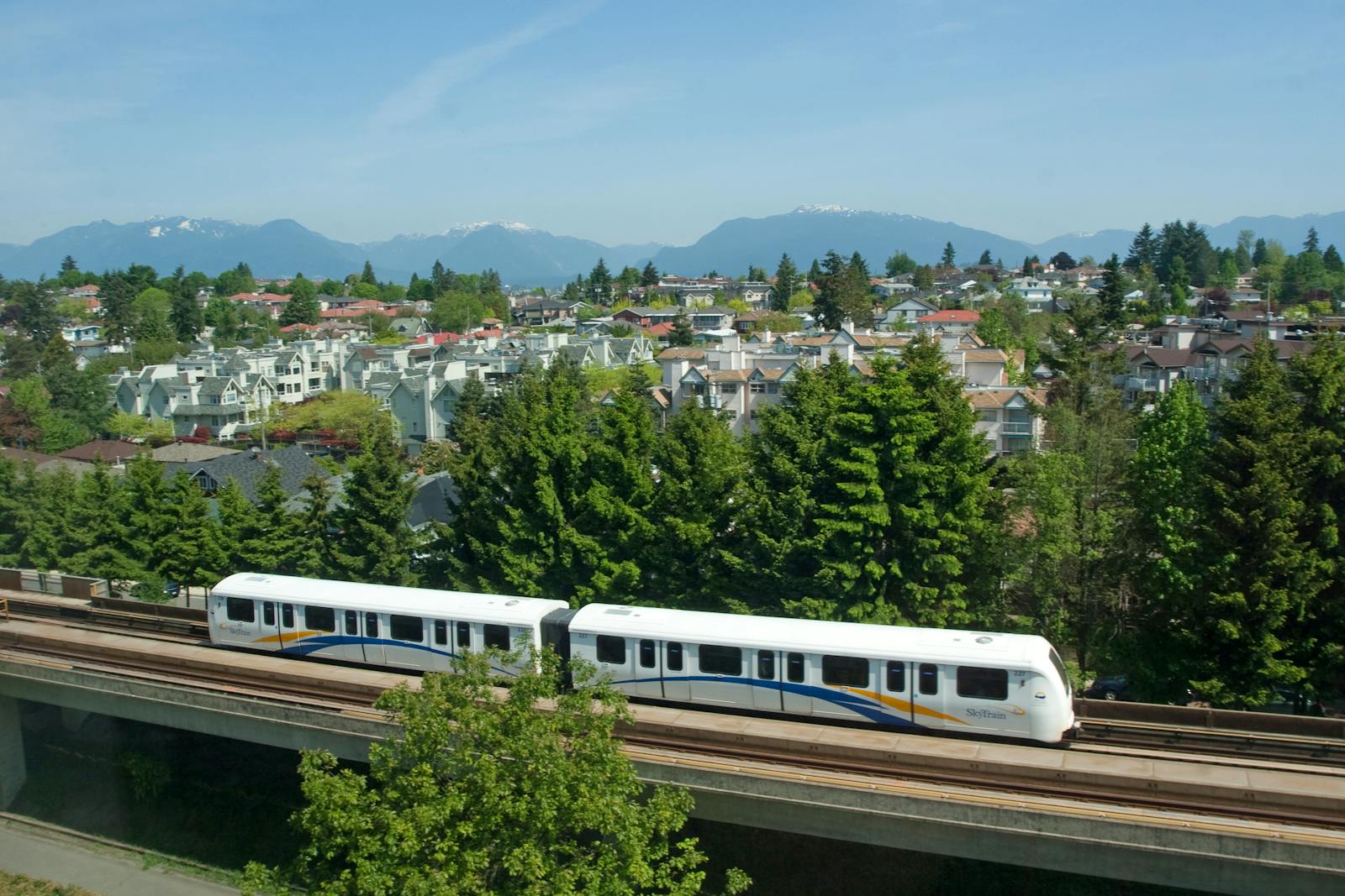 SkyTrain crossing Vancouver suburbs with mountain backdrop, Lower Mainland BC