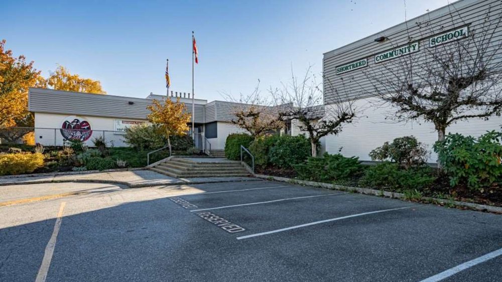 Front of Shortreed Community School on a sunny autumn day, with green lettering on the building, a circular painted mural, flagpoles, entry stairs and an empty parking lot