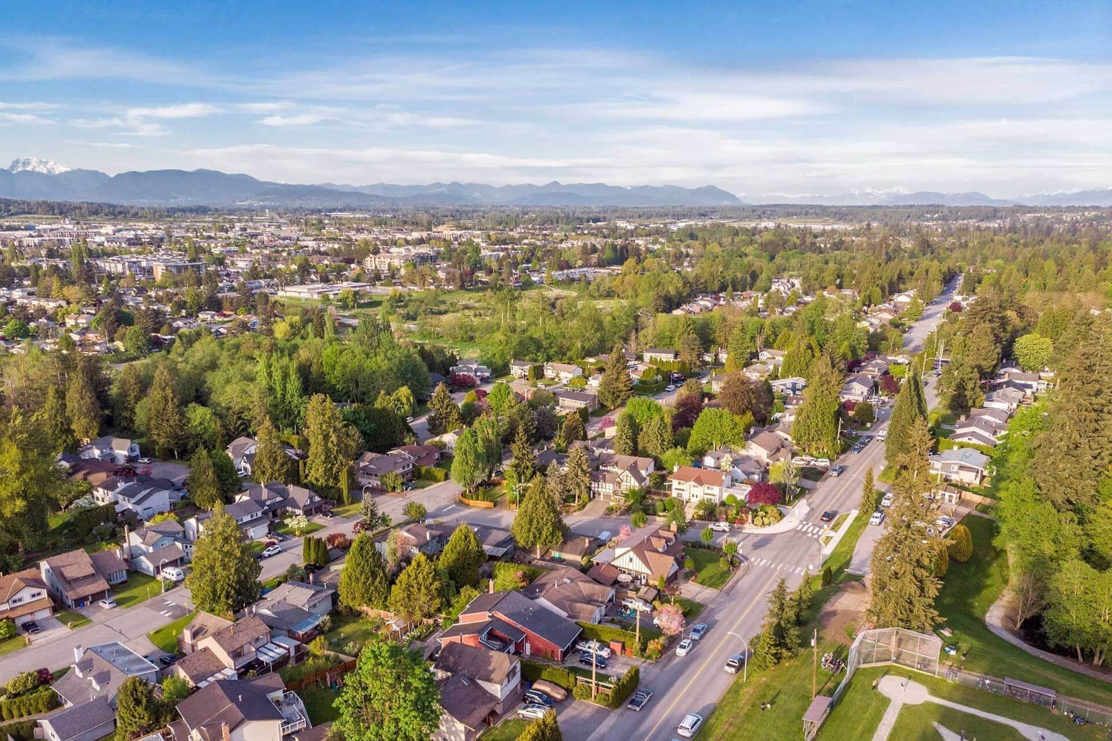 Aerial view of homes and a ball diamond in Langley City, with the mountains beyond