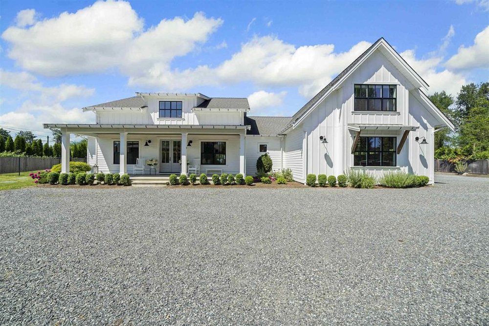 A white modern farmhouse with a covered porch and a gravel driveway in Glen Valley