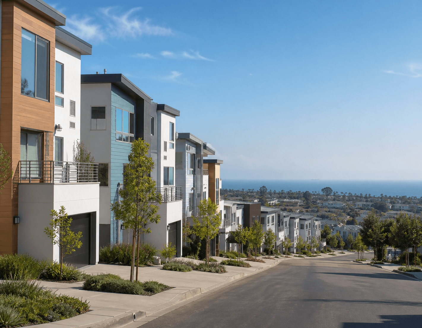 Sunlit hillside street of contemporary townhomes in Signal Hill with a hazy ocean view on the horizon