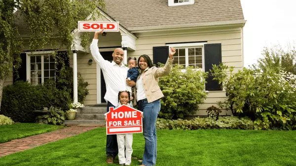 Happy family celebrating in front of their new home with SOLD and For Sale signs on the lawn in Southern California