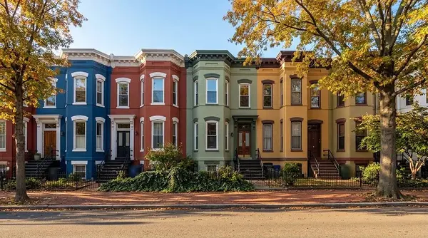 A row of colorful painted brick rowhouses with front stoops and iron railings on a Washington DC street in autumn