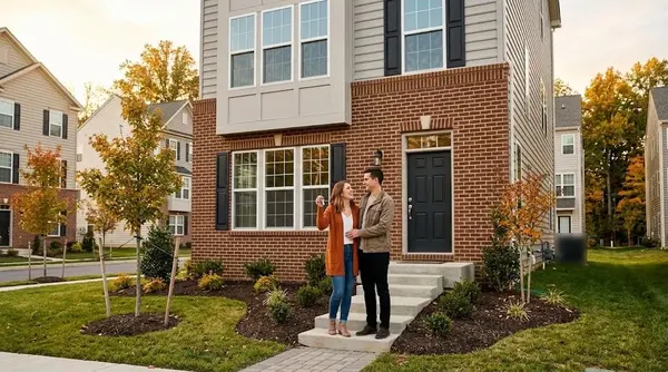 Young couple holding new house keys on the front steps of a brick townhome in Northern Virginia