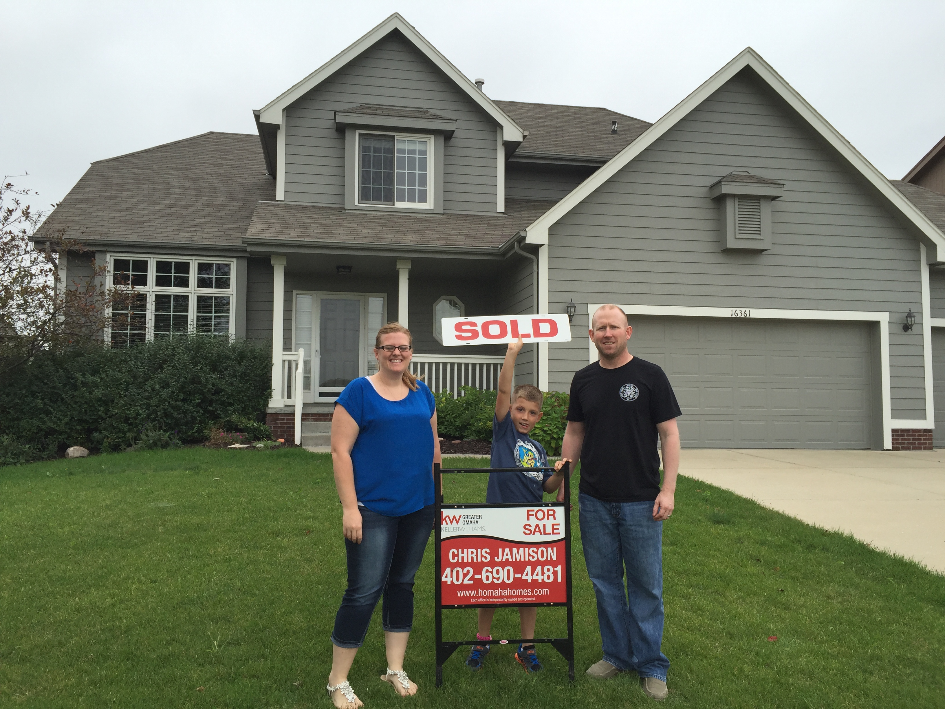Family standing in front of their home with a Sold sign after buying their next house before selling in Omaha.