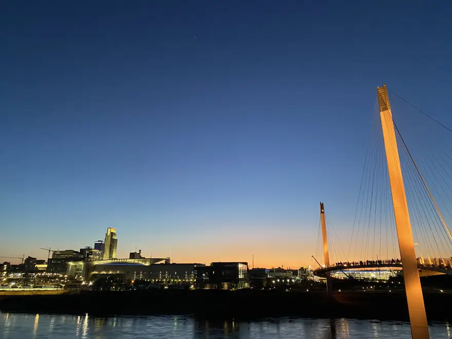 Downtown Omaha skyline at dusk with the lighted Bob Kerrey Pedestrian Bridge over the Missouri River