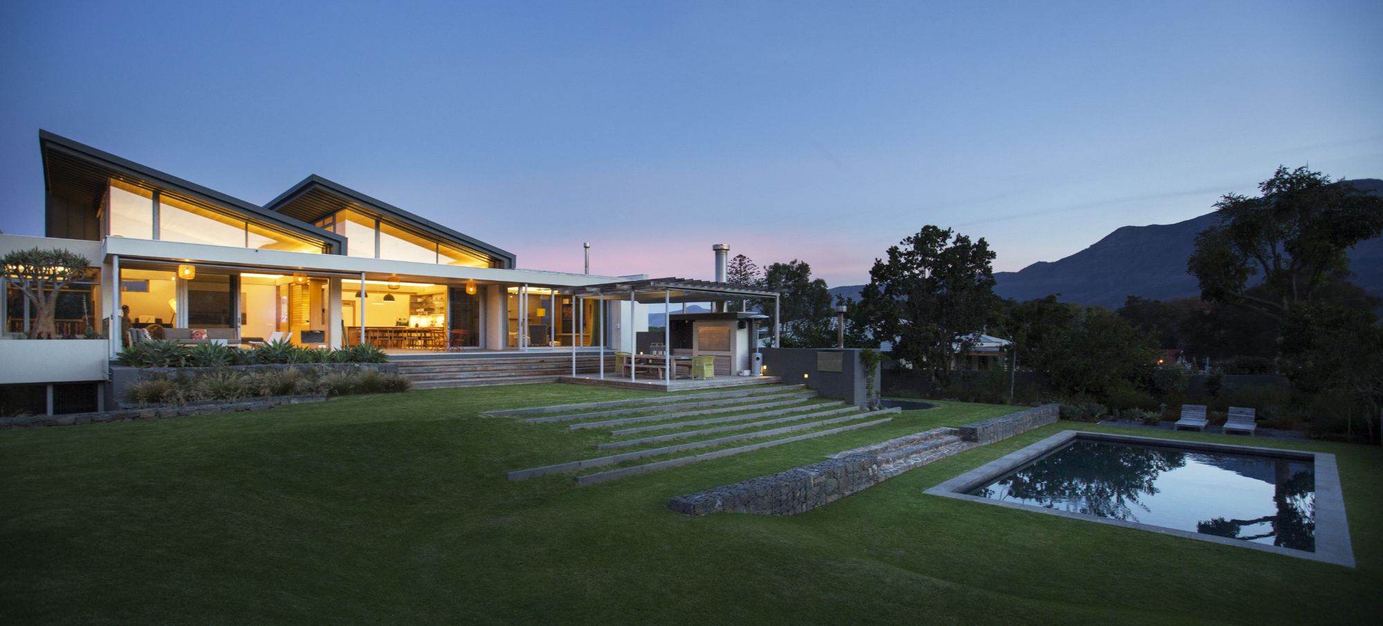 Illuminated modern house beyond yard and swimming pool at night