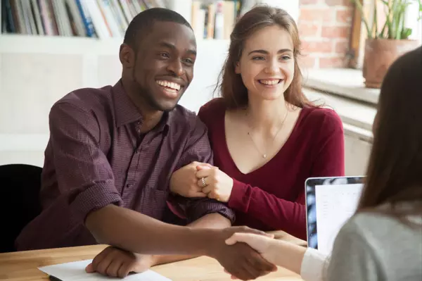 Smiling multiracial couple customers shaking hands with mortgage broker or financial advisor