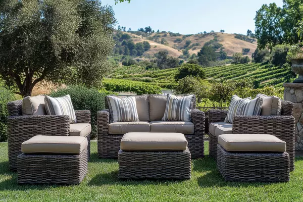 Olive-brown wicker outdoor furniture set with two armchairs, three single chairs with ottomans, and a coffee table on a patio overlooking California wine country hills.
