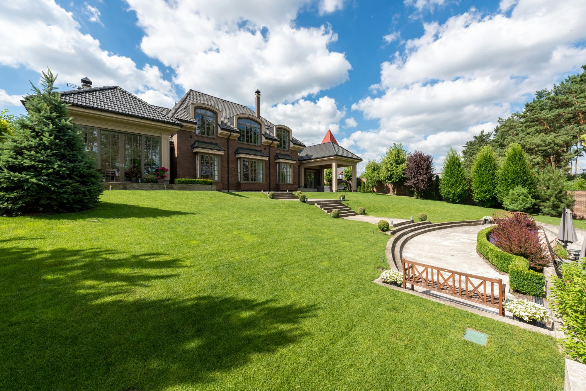 Discover this stunning brick estate with expansive lawns, manicured landscaping, and a covered patio. Featuring large windows, a classic chimney, and stone steps leading to a terrace, this home blends timeless elegance with modern comfort.