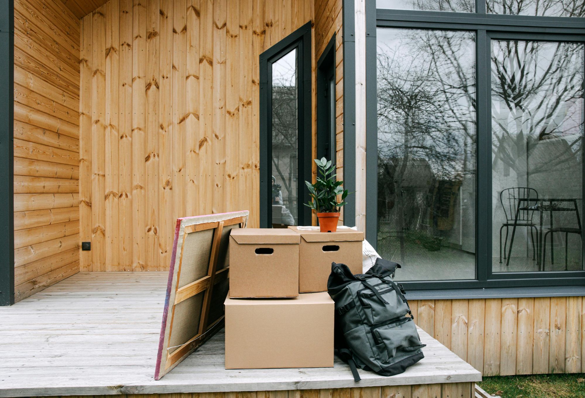 Modern Boulder, CO house porch with stacked moving boxes, backpack, potted plant, and framed canvas, symbolizing relocation or new homeowners.