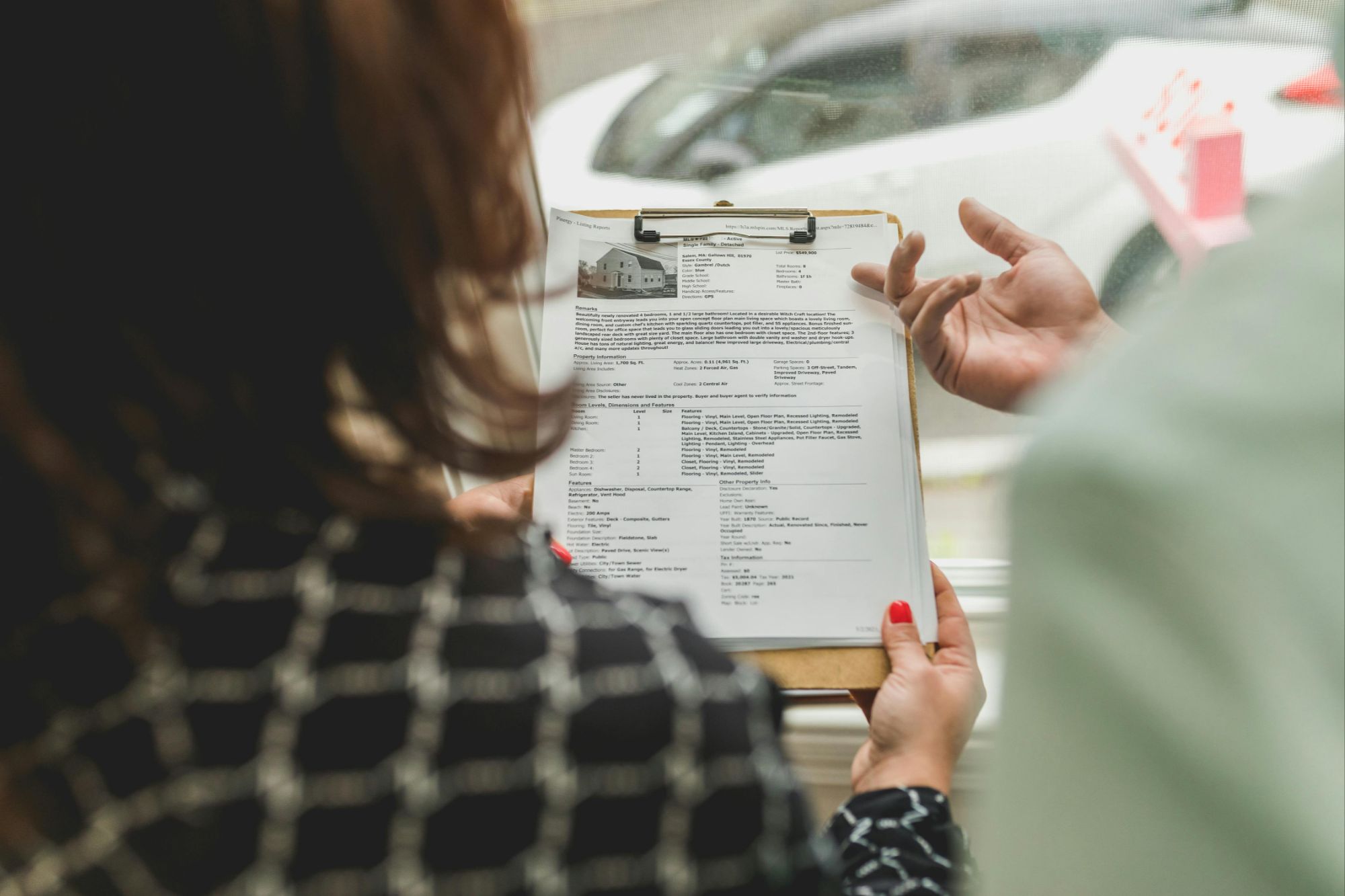 A Boulder real estate agent reviewing detailed property listing documents on a clipboard with a client during a home valuation or refinancing consultation.